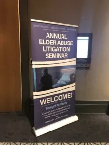 A photo of a Welcome Sign in front of a door. The sign says "Annual Elder Abuse Litigation Seminar. Welcome."